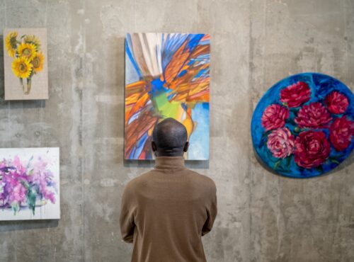 Back view of African male guest of art gallery standing in front of wall with expositions