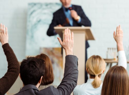 back view of buyers raising hands to auctioneer during auction
