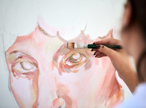 Young girl artist draws with paint brush man portrait on white canvas at art painting festival
